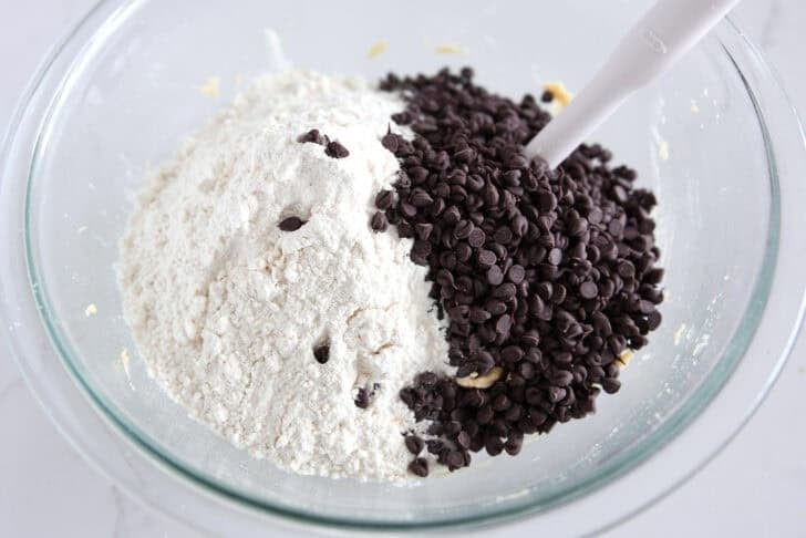 Glass bowl with cookie dough, white flour, and mini chocolate chips.