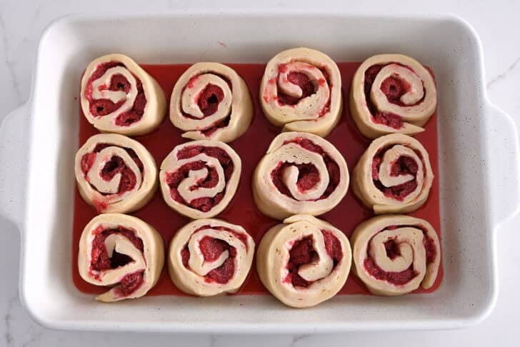 White 9X13-inch pan with rising raspberry sweet rolls.