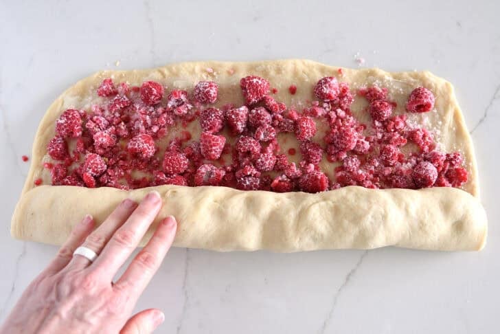 Rolling up log of raspberry sweet rolls with sugary raspberry filling.