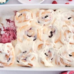 White 9X13-inch pan of baked raspberry sweet rolls spread with sweet cream cheese icing.