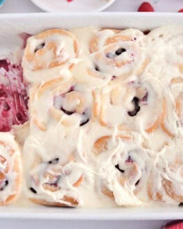 White 9X13 inch pan of Baked Raspberry Sweet Rolls topped with sweet cream cheese icing.