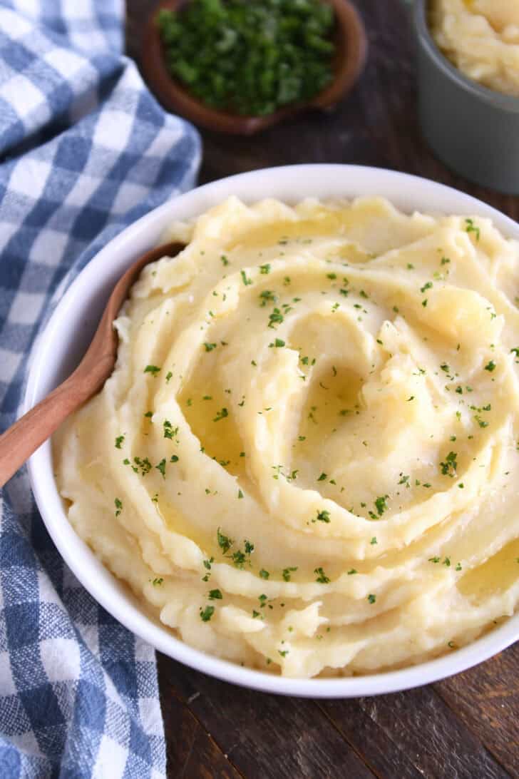 Top down view of a white bowl with creamy mashed potatoes topped with parsley flakes.