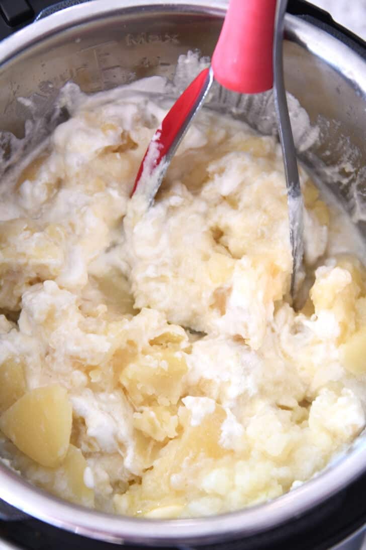 Top down view of an Instant Pot with mashed potatoes and sour cream getting mashed.