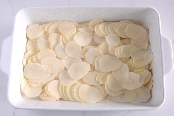 White 9X13-inch dish layered with thin potatoes.