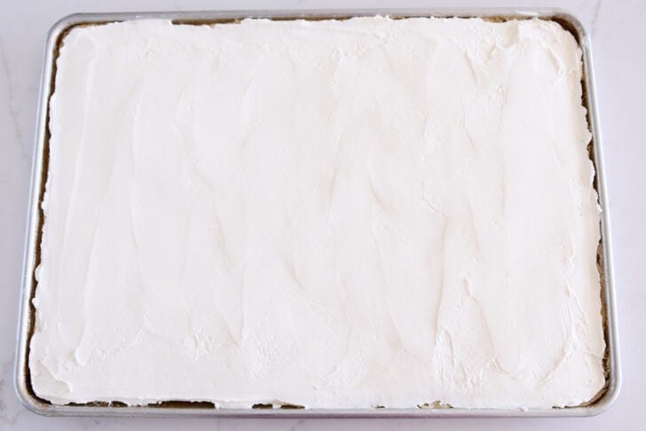 White sheet cake in half sheet pan topped with cream cheese layer.