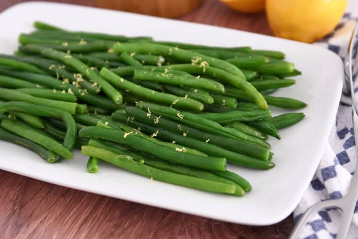 White tray with cooked green beans sprinkled with lemon zest.