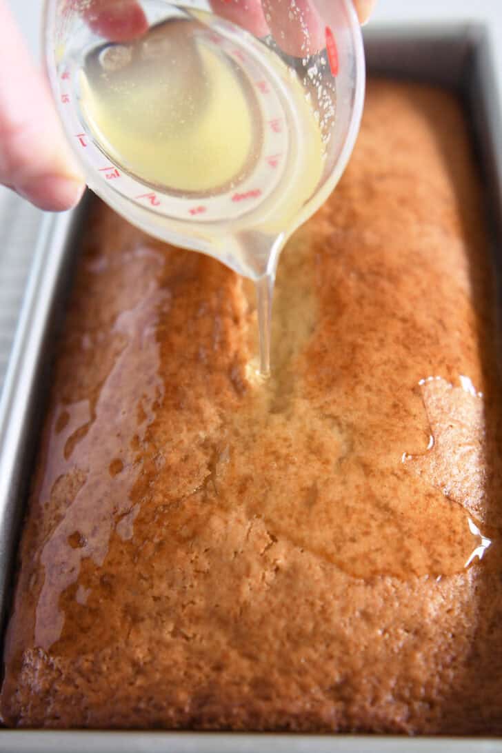 Pouring lemon glaze over baked lemon bread in metal loaf pan.