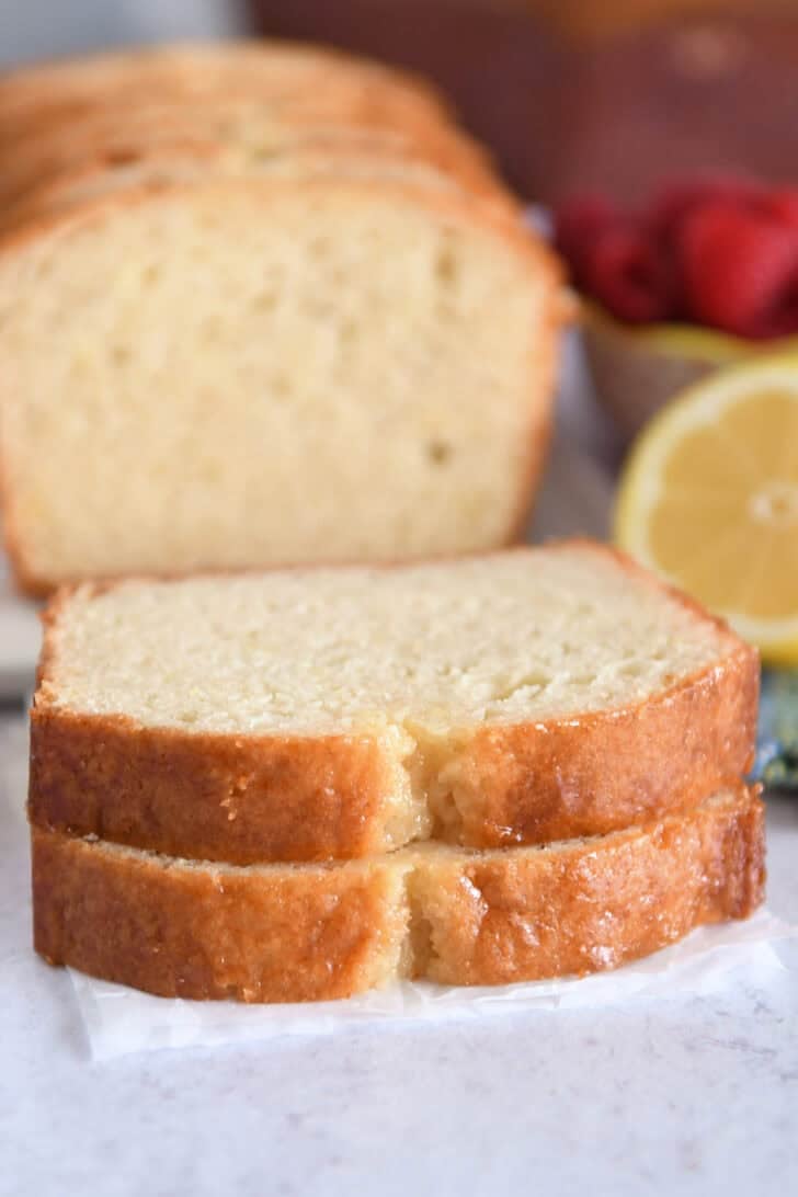 Two slices of lemon quick bread stacked on parchment paper.