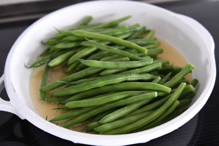 White skillet with broth and fresh, uncooked green beans.