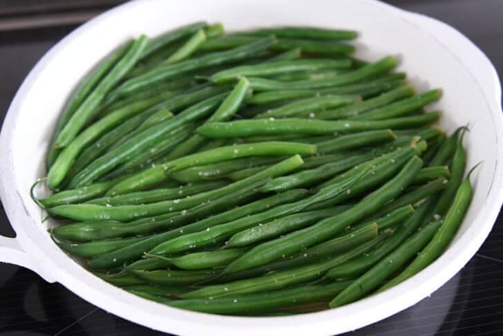 Place broth, cooked green beans, and salt in a white skillet.