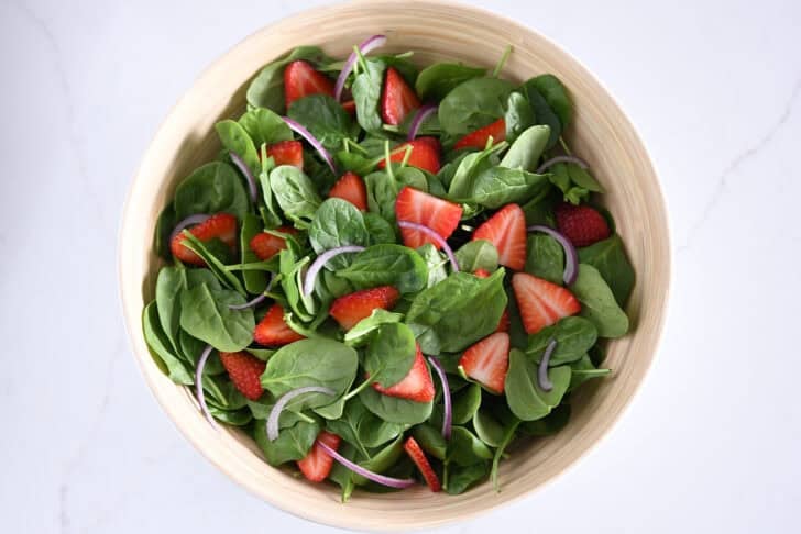 Wooden salad bowl with fresh spinach, sliced strawberries and sliced red onions.