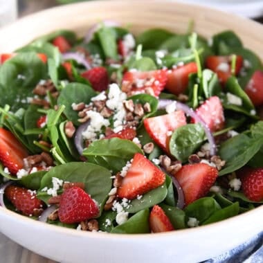 Wooden salad bowl with fresh spinach, sliced strawberries, sliced red onions, feta cheese, chopped pecans and poppy seed dressing.