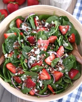 Wooden salad bowl with fresh spinach, sliced strawberries, sliced red onions, feta cheese, chopped pecans and poppy seed dressing.