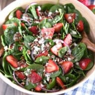 Wooden salad bowl with fresh spinach, sliced strawberries, sliced red onions, feta cheese, chopped pecans and poppy seed dressing.