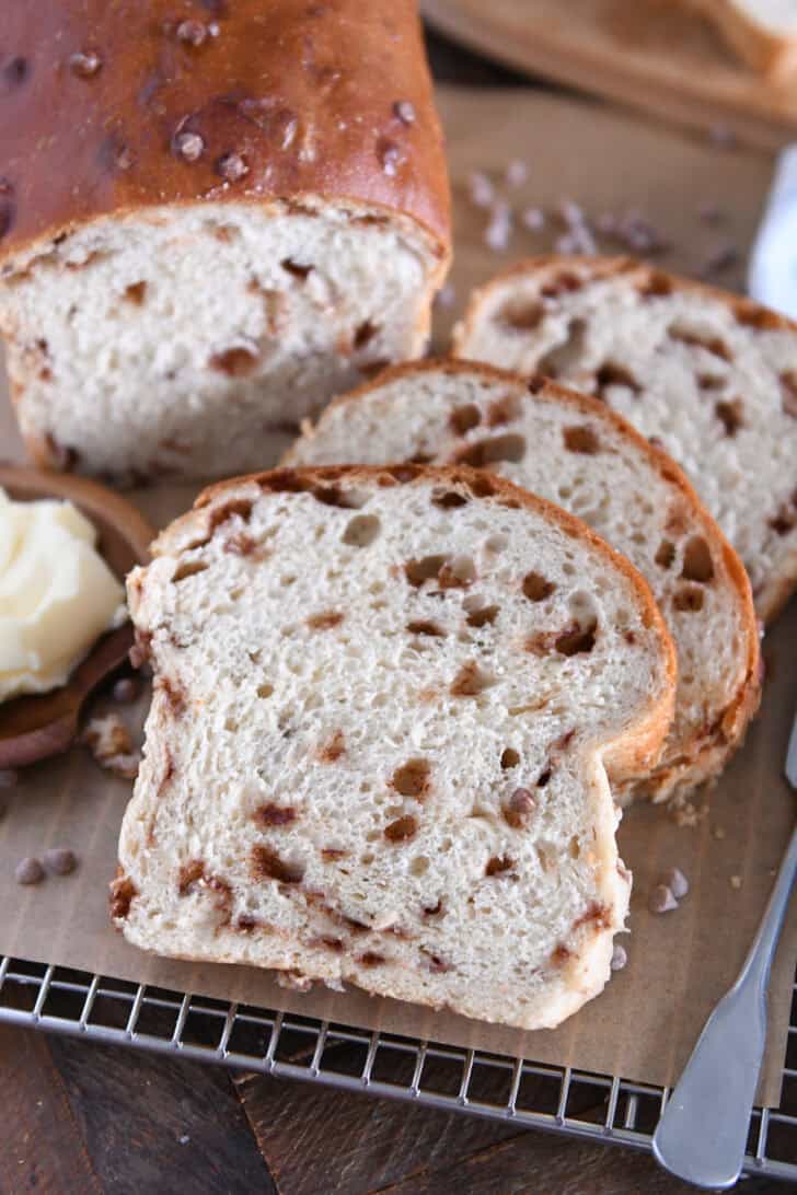 Slice of cinnamon burst bread on brown parchment paper with butter on wooden dish to the side.