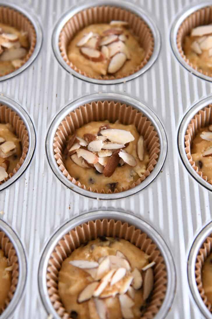 Place unbaked almond coconut chocolate chip muffin batter in muffin tins and top with sliced ​​almonds.