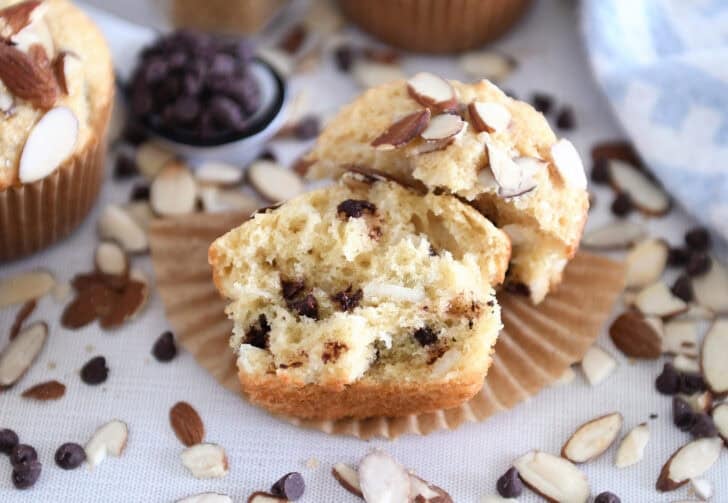 1 almond coconut chocolate chip muffin, broken in half, on brown paper liner.