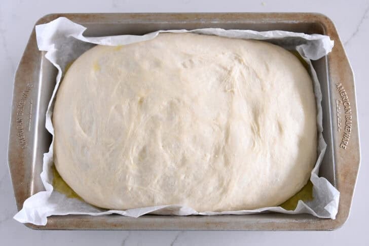 Let the unbaked focaccia bread rise in a 9X13 inch baking pan lined with parchment paper.
