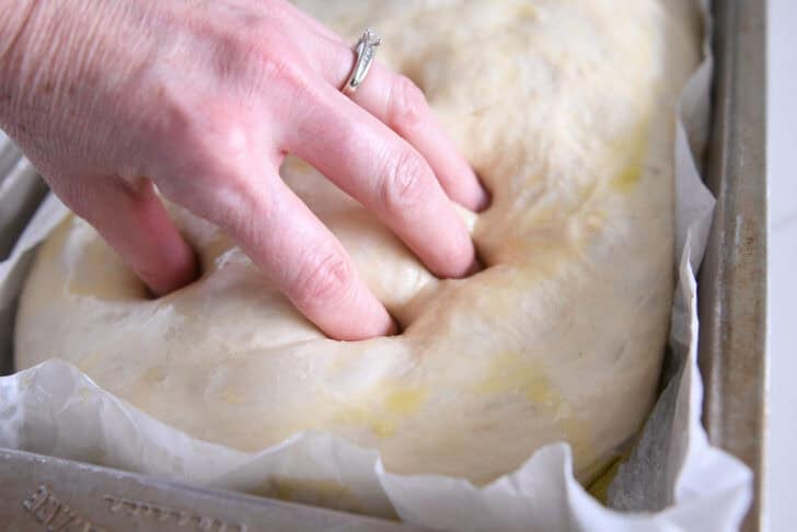 Use your fingers to press into the dimples of the unbaked focaccia bread topped with olive oil.