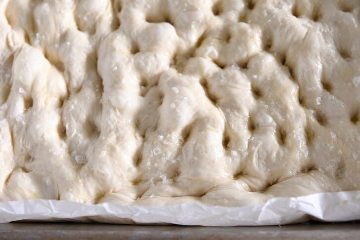 Unbaked focaccia dough in a 9X13 inch pan lined with parchment paper.