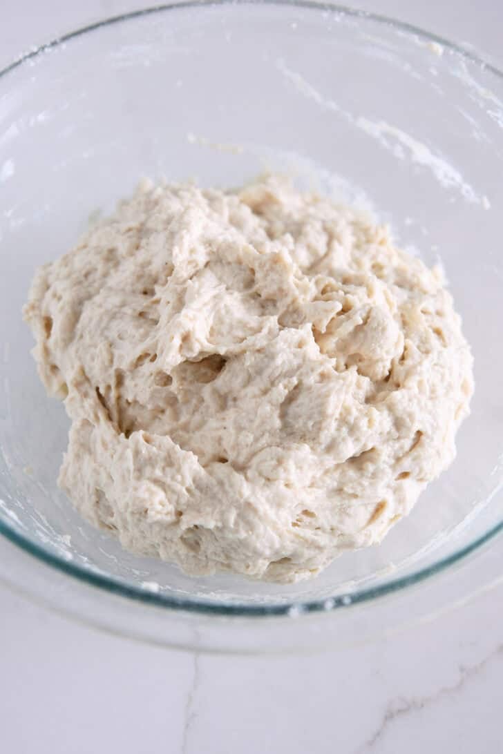 Shaggy mixture of focaccia dough in a glass bowl.