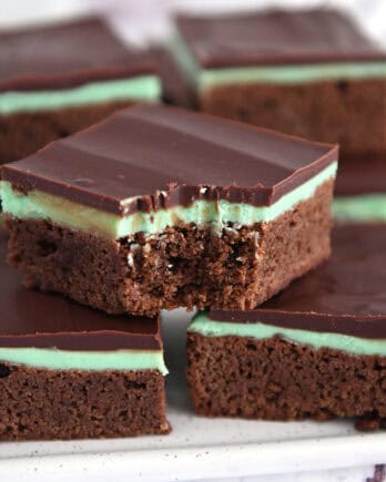 White tray of squares of chocolate mint brownies with top brownie with bite taken out.