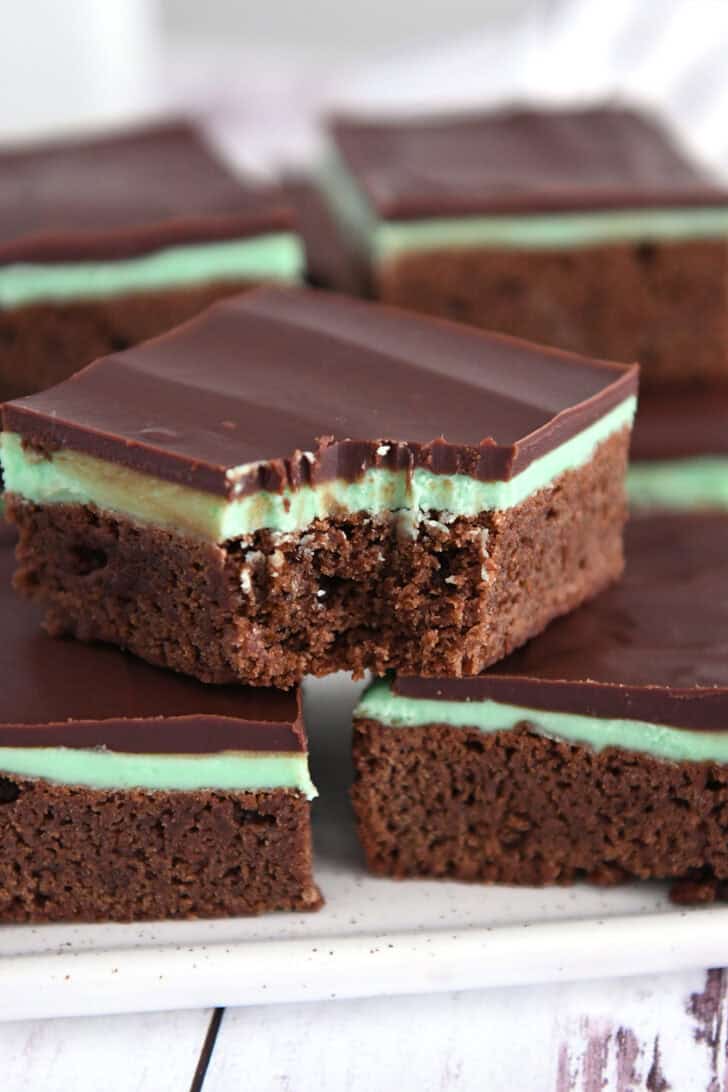White tray of squares of chocolate mint brownies with top brownie with bite taken out.