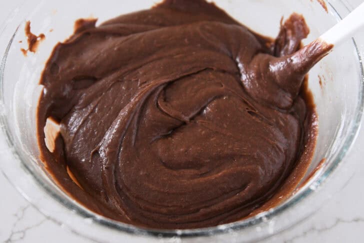 Glass bowl with thick brownie batter and white spatula.