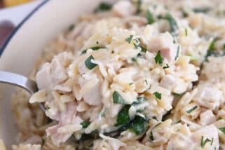 Serving spoon with scoop of creamy orzo, spinach and chicken.