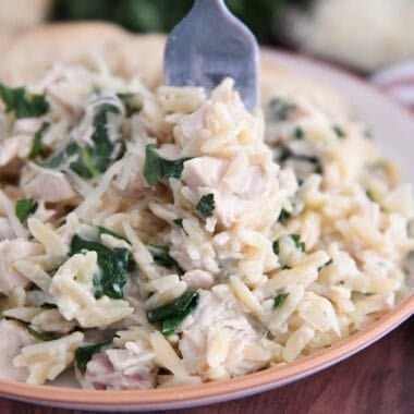 Creamy orzo with spinach and chicken on white plate with fork.