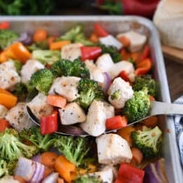 Serving spoon with cooke chicken, broccoli, carrots, bell peppers and red onions.