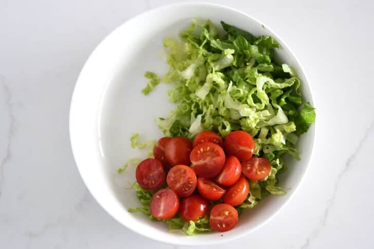 Lettuce and tomatoes in a white bowl, top down view.