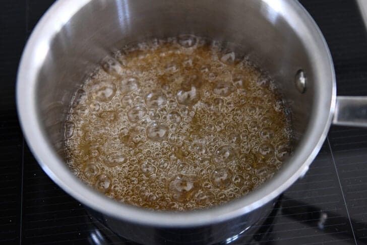 Sugar and water simmering in saucepan and turning golden brown in color.