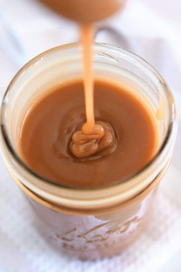 Drizzling caramel sauce from spoon into glass jar.