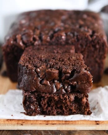 Two half slices of chocolate banana bread stacked on white parchment paper.