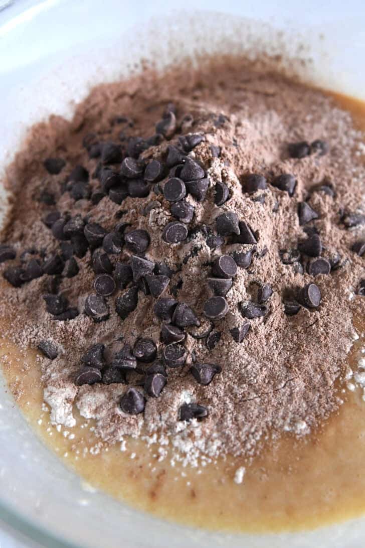 Glass bowl with banana bread dough, cocoa powder and chocolate chips.