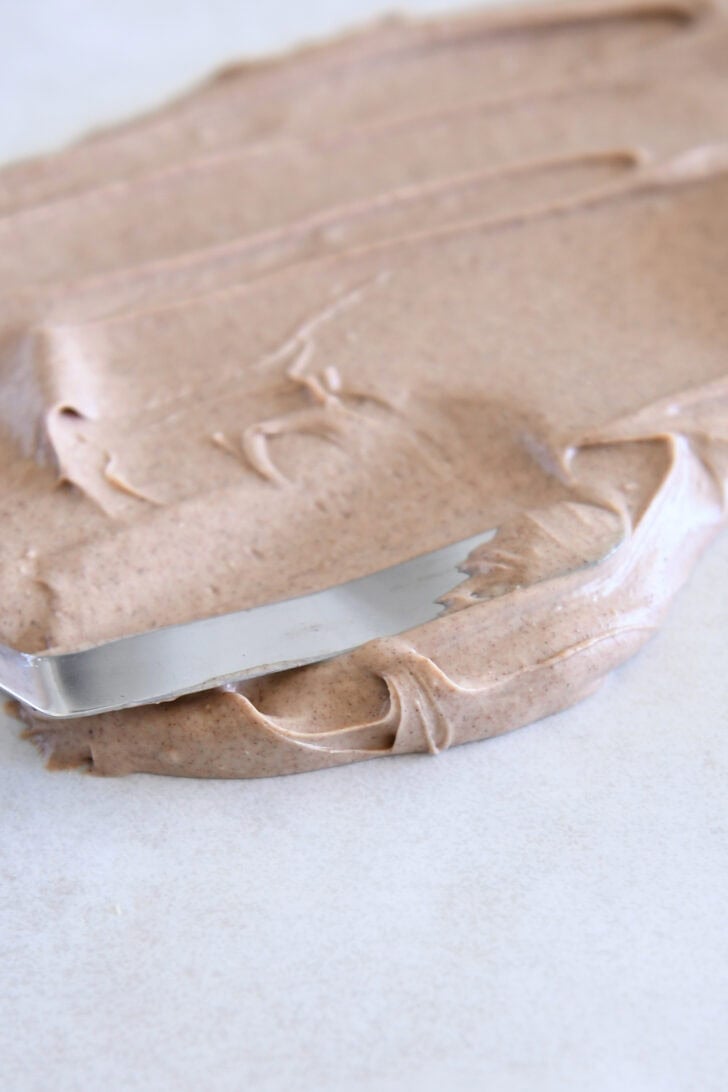 Spreading cinnamon white chocolate mixture on parchment paper with offset spatula.