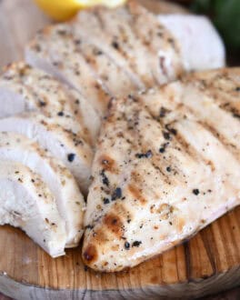 Grilled chicken breast on wood platter with sliced chicken.