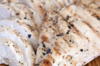 Grilled chicken breast on wood platter with sliced chicken.