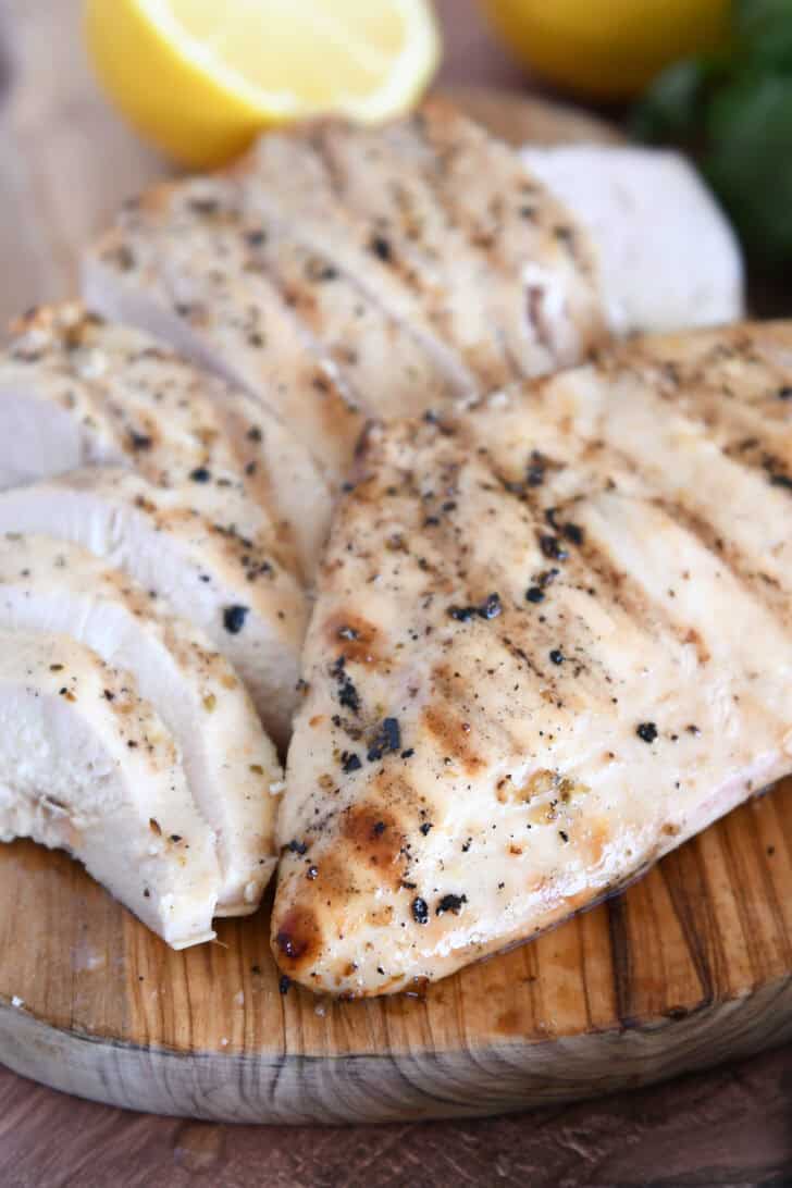 Grilled chicken breast on wood platter with sliced chicken.