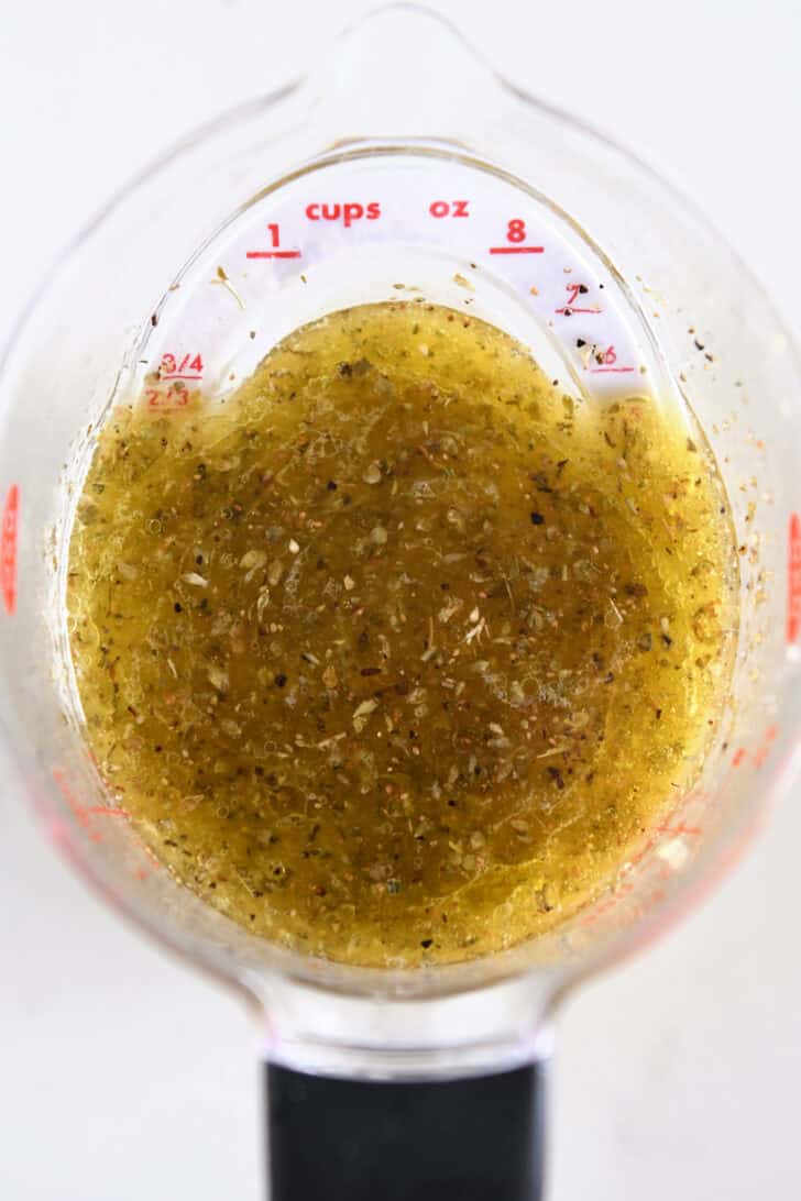Liquid measuring cup with olive oil, lemon juice, garlic, oregano and salt.