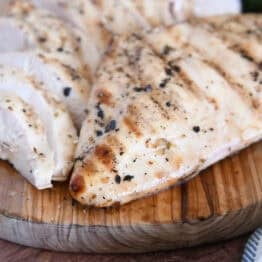 Grilled chicken breast on wood platter with sliced chicken breasts.