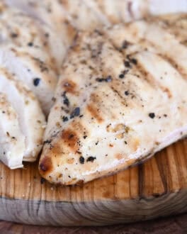 Grilled chicken breast on wood platter with sliced chicken breasts.