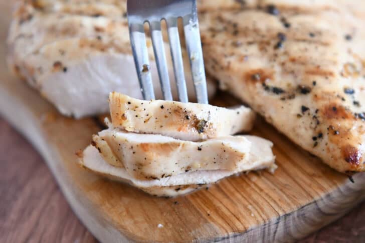 Fork piercing three pieces of lemon garlic grilled chicken.