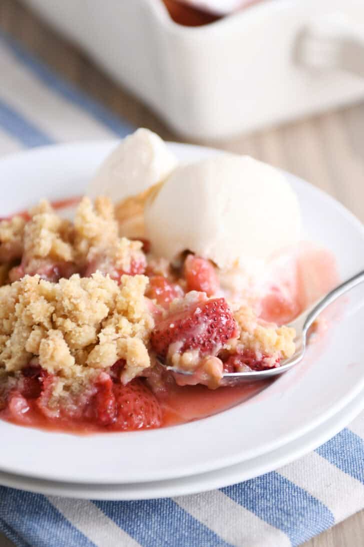 White plate with serving of strawberry rhubarb crumble and vanilla ice cream.