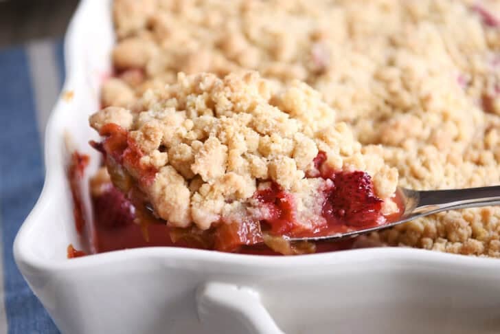 White pan with scoop of strawberry rhubarb crumble on serving spoon.
