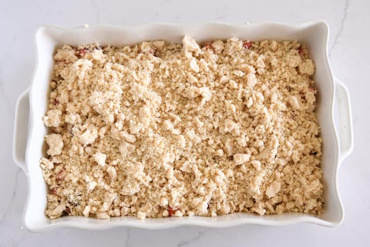 White pan with unbaked strawberry rhubarb crumble with streusel topping.