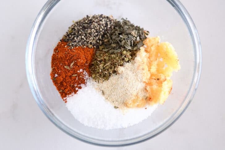 Salt, onion powder, fresh garlic, oregano, basil, pepper and smoked paprika in glass bowl.