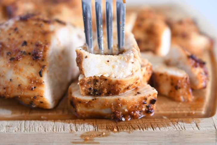 Fork piercing three pieces of air fryer chicken breasts.