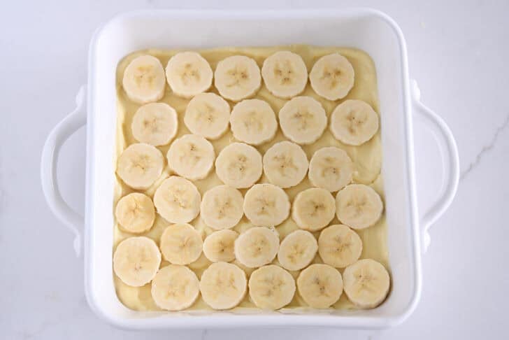 White square 8X8 baking dish with layer of vanilla pudding and sliced bananas.